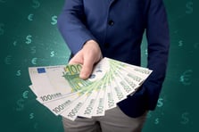 Young businessman holding large amount of bills with green background and currency symbols